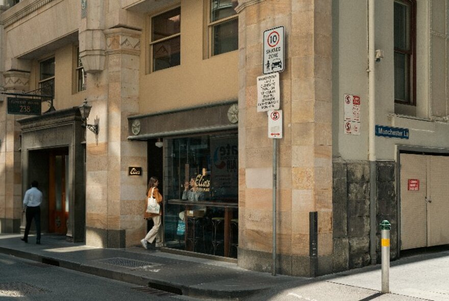 A person walking into an open doorway of a cafe in an Edwardian-style sandstone building.