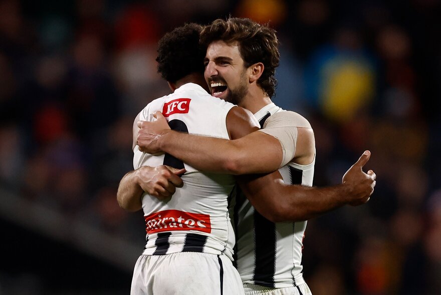 Collingwood AFL football players hugging during a match.
