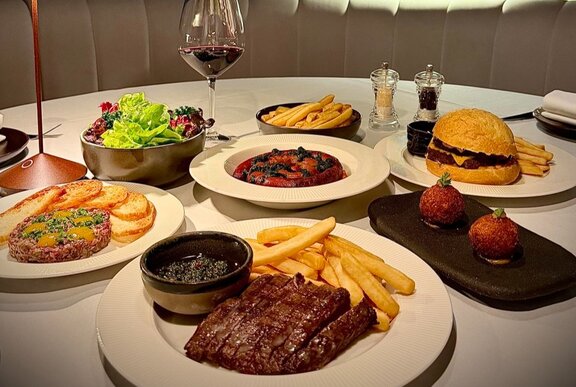 A spread of woodfired steaks, chips, salads, and drinks on a restaurant table.