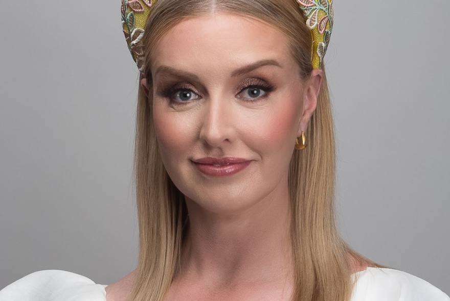 A headshot of a woman wearing a fascinator head band. 