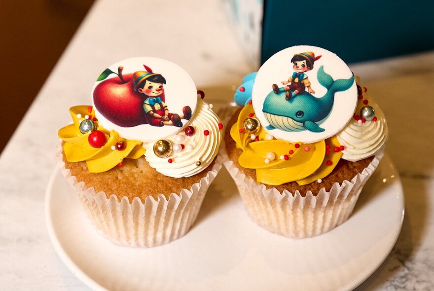 Two cupcakes on a plate decorated with Pinocchio imagery.