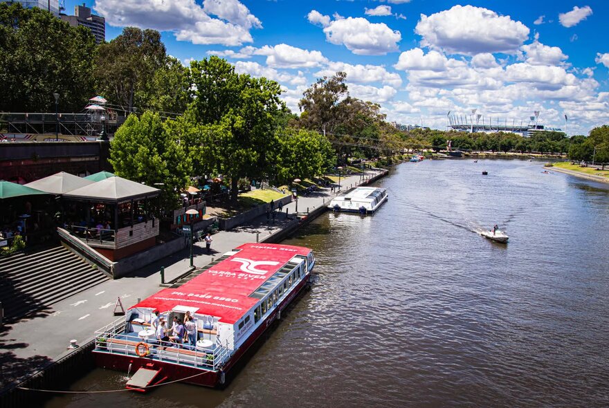 Aerial view of a river cruise boat with a red roof moored on the Yarra river. 