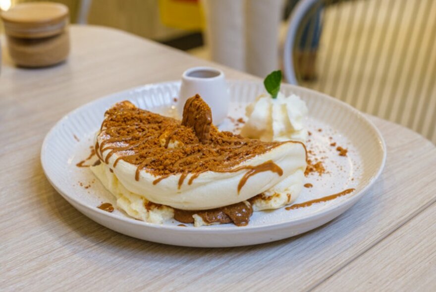 Pancake on a white plate covered in syrup and biscuit toppings. 