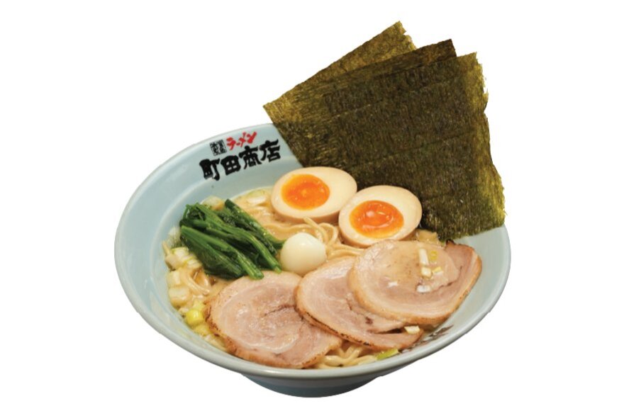 A white bowl of ramen from the Japanese chain Machida Shoten, with sliced pork, hard boiled eggs and noodles sitting on top of broth.
