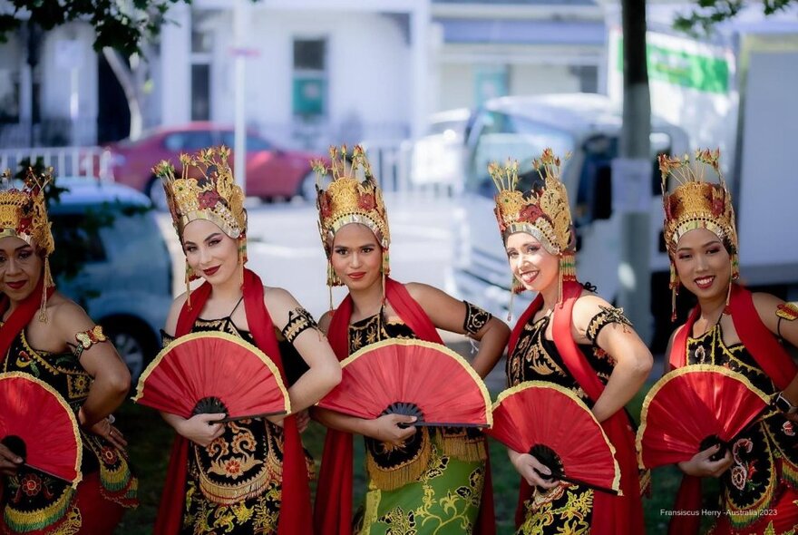 Indonesian dancers wearing headdresses and holding red fans.