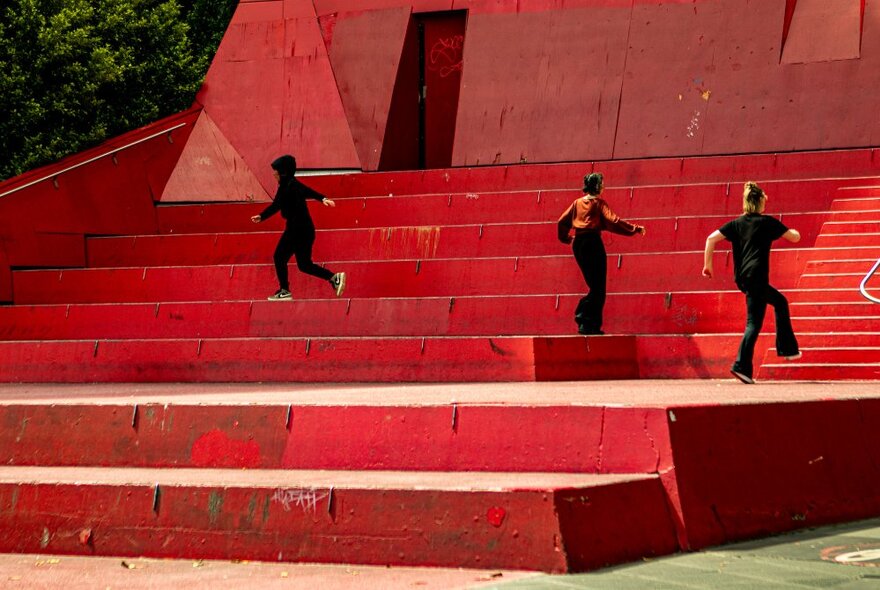 Three performers on a large outdoor red stairs.