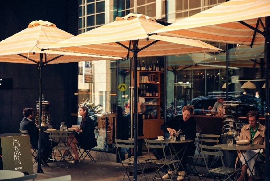 Outdoor diners under three peach coloured striped umbrellas
