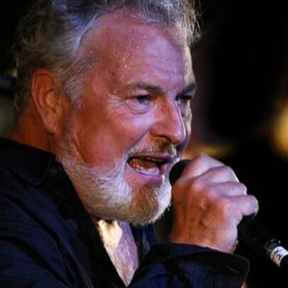 Closeup side profile of middle-aged male singer Ross Wilson, singing into a microphone he holds in his hand.