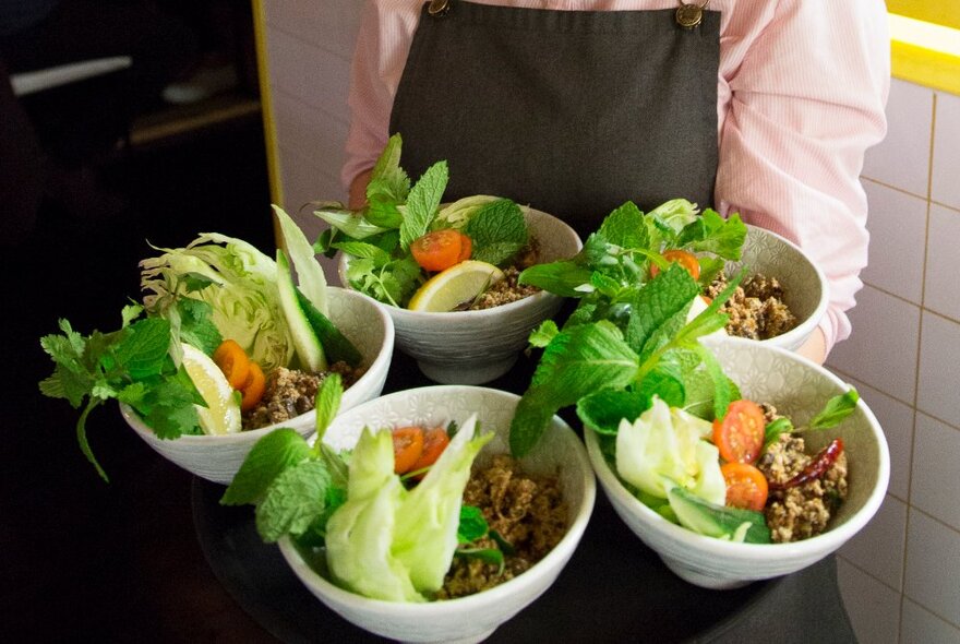 A waiter carrying a tray of four identical dishes, all with vegetables and herbs.