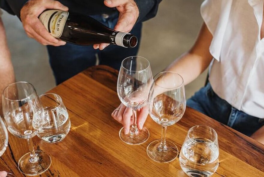 A hand pouring wine into empty glasses.