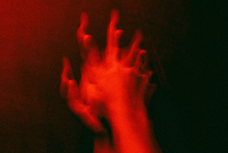 A blurred image of two clasped hands, with a red filter overlaid.