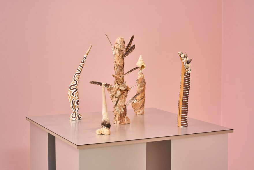 Display of totemic sculptural pieces on a table in a gallery setting.