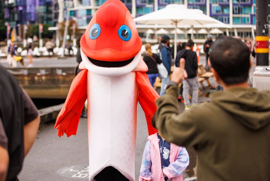 Person photographing a child with a seafood-themed character.