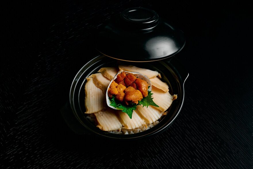 A black pot with the lid off revealing a small meat dish. 
