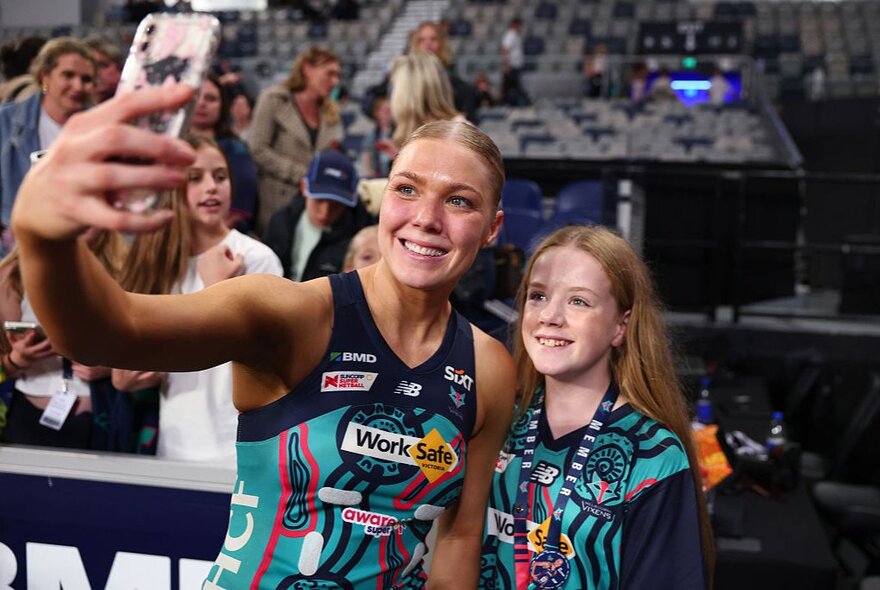 Netball player taking a selfie with a young fan wearing team colours.