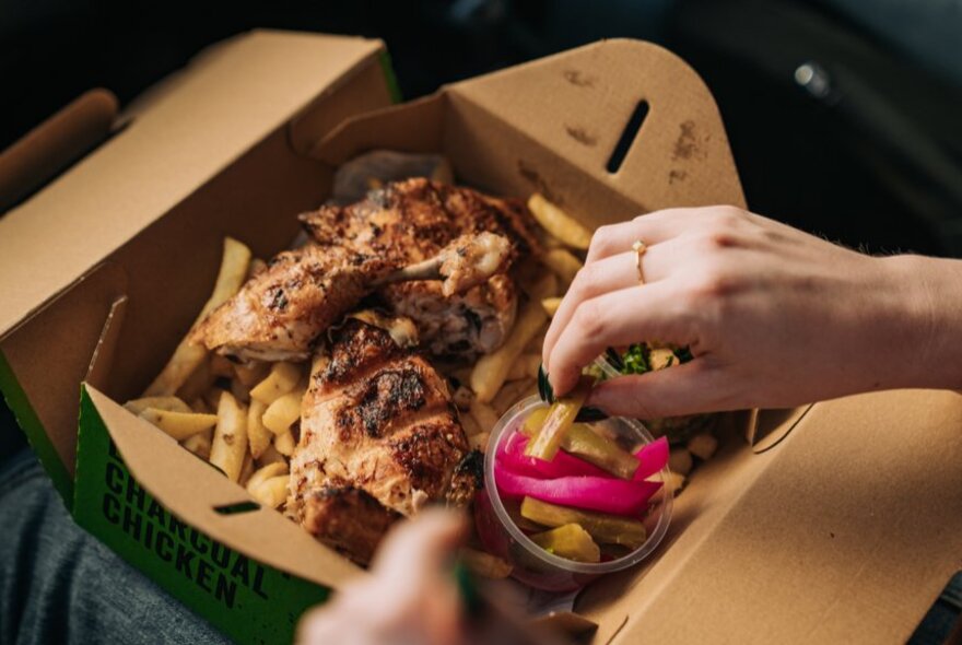 Hands holding a cardboard box full of chicken with dip.