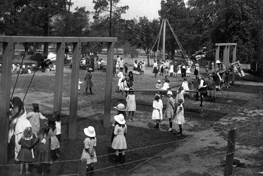 Black and white photo of children at the playground featuring swings and seesaws