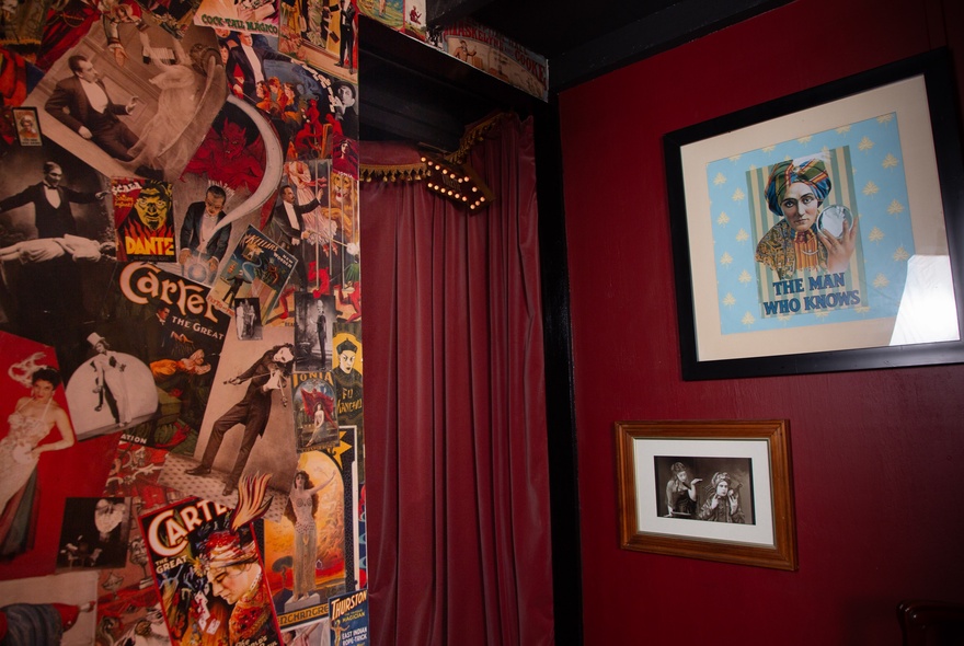 The interior foyer of Piccolo Teatro, with a wall papered with magician images and the pink velvet curtain seen through the entry to the stage room.