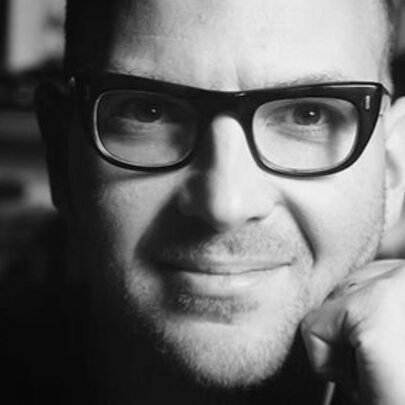 Author Cory Doctorow wearing heavy dark-rimmed spectacles, resting his head on his fist.