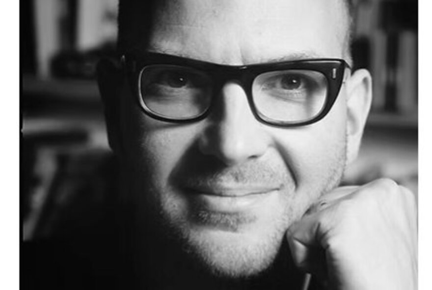 Author Cory Doctorow wearing heavy dark-rimmed spectacles, resting his head on his fist.