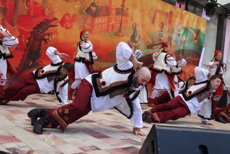 Polish dancers in traditional red, white and black attire, dancing on stage.