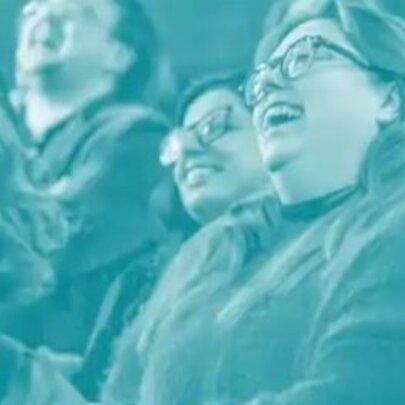 People wearing spectacles seated in rows, laughing.