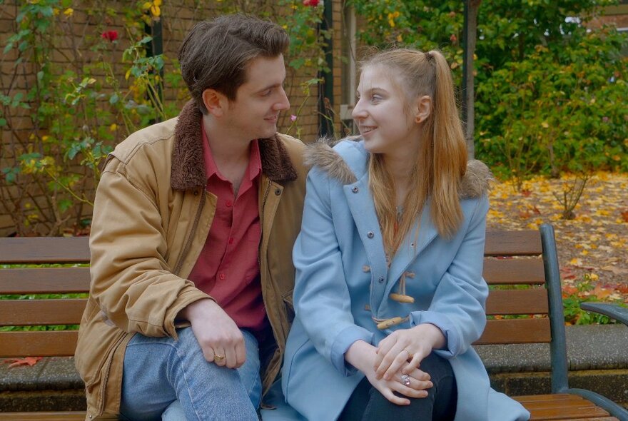 Film still from a movie depicting two people seated next to each other on a park bench.