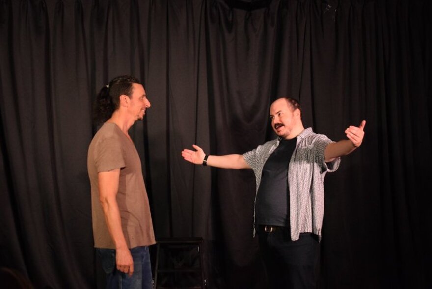 Two actors improvising on a stage in front of an black curtain.
