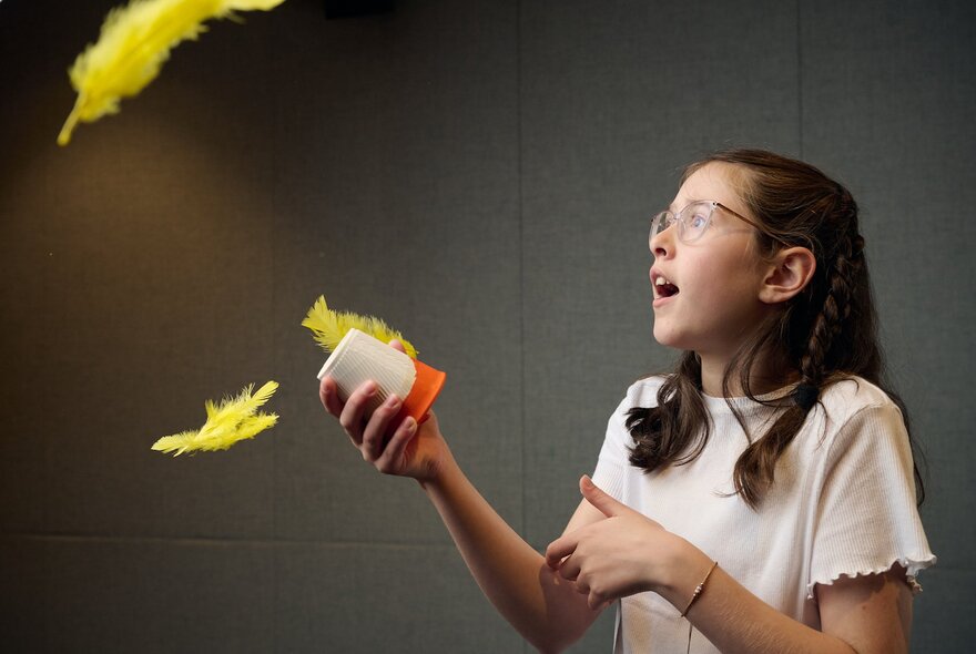 A young girl holding a canister while yellow feathers waft in the air.