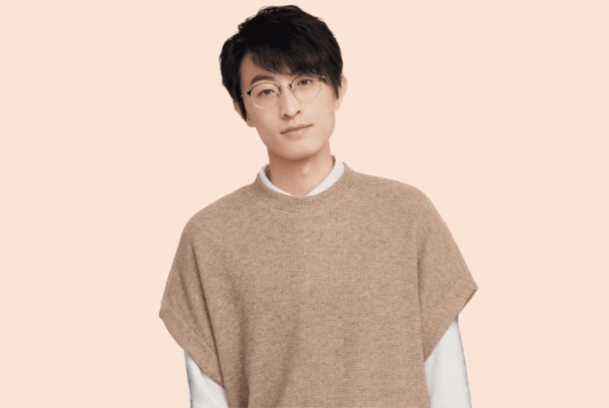 Chinese comedian, Qiu Rui, wearing a beige woolen sleeveless jumper over a white long sleeve t-shirt.