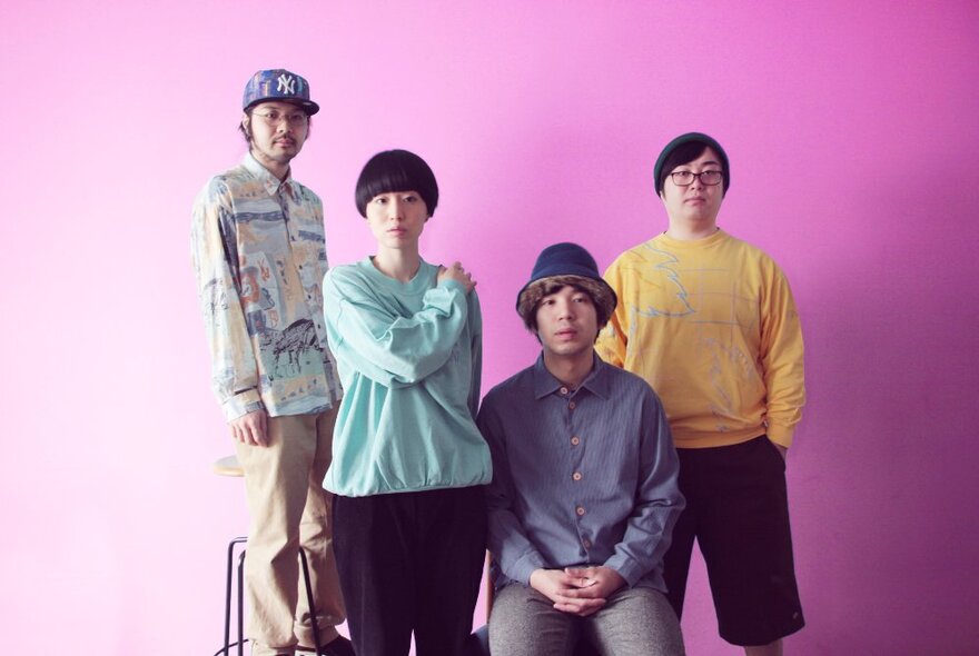 Four members of a band, posed against a pink wall.