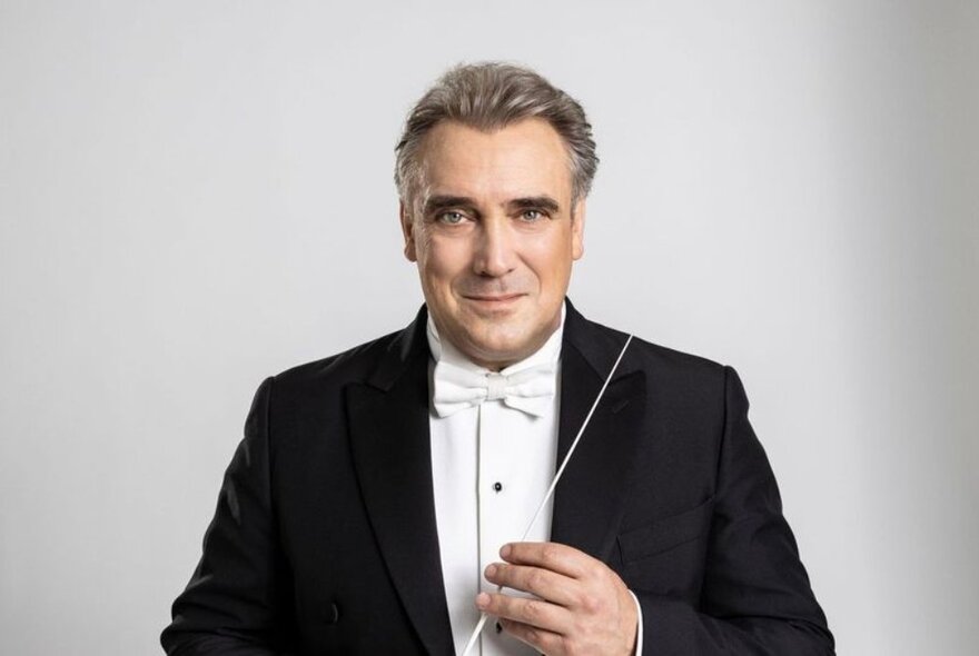 The MSO conductor Jaime Martín wearing a tuxedo, holding a baton in his hand, and posed against a white background.