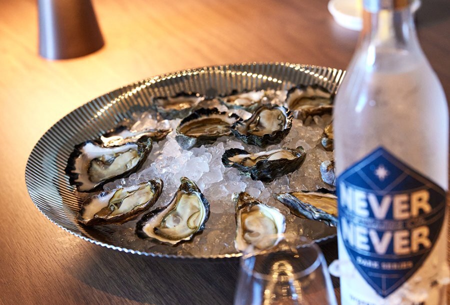 A tray of oysters on ice with a gin bottle in the foreground.