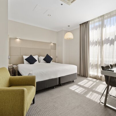 Hotel suite with green sofa and beige bed, drapes and carpet.