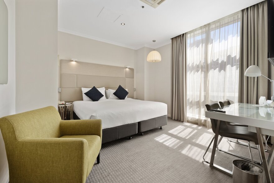 Hotel suite with green sofa and beige bed, drapes and carpet.