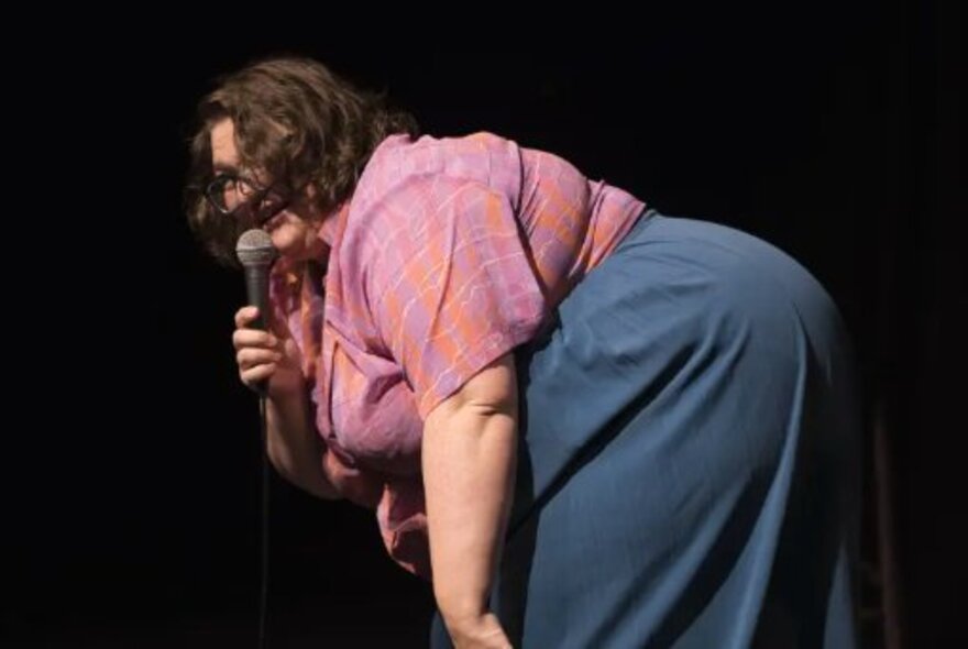 Large woman leaning over while speaking into a microphone.