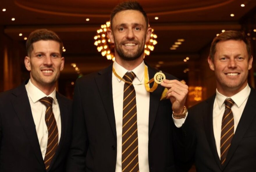 Three AFL footballers, one holding a medal around his neck.
