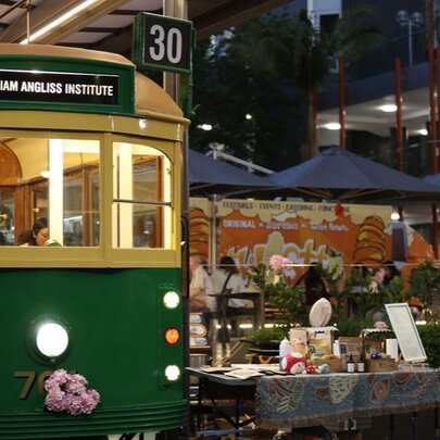 Vintage Melbourne tram parked next to an outdoor market stall at night.