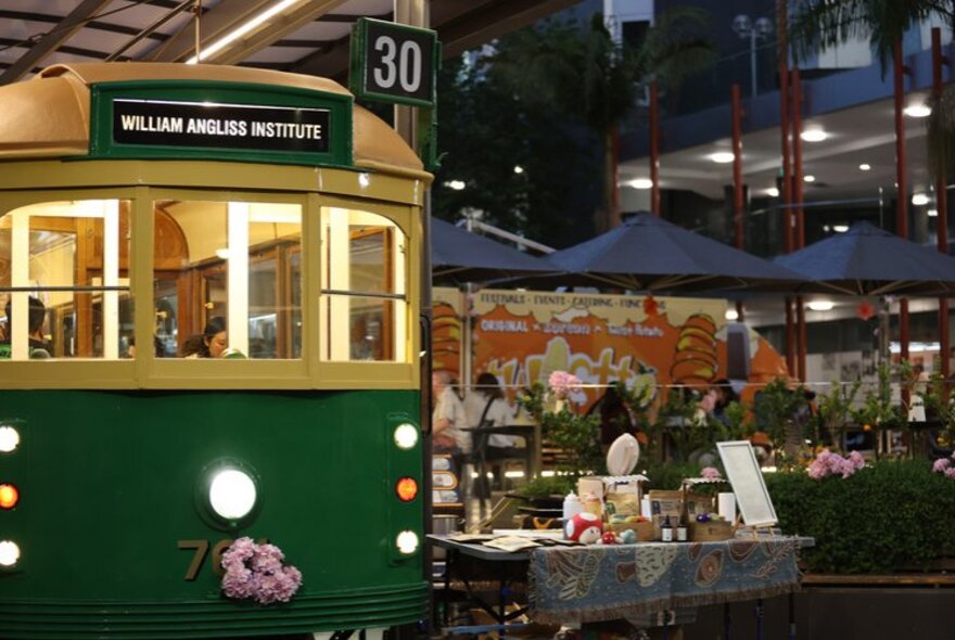 Vintage Melbourne tram parked next to an outdoor market stall at night.