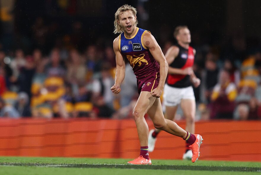 A Brisbane Lions AFL player cheering himself on with pumped fists, while running on the footy field.