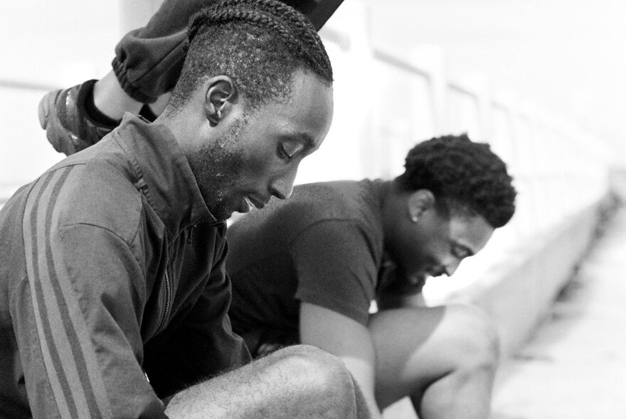 Photojournalism image of two men seated while tieing their shoes.