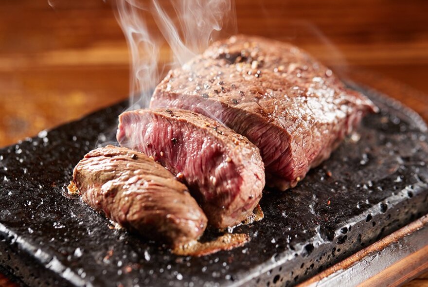 A steak cooking on a hot lava stone plate, sliced to show the grain of the meat.