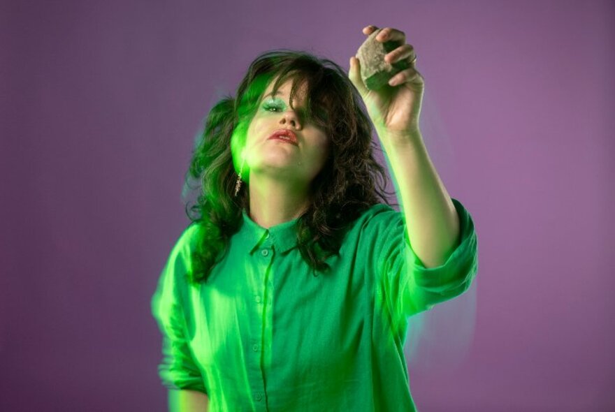 Comedian wearing green eye makeup and shirt, holding rocks in her hands.