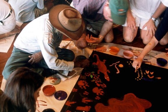 People gathered around an Elder teaching Indigenous painting skills.