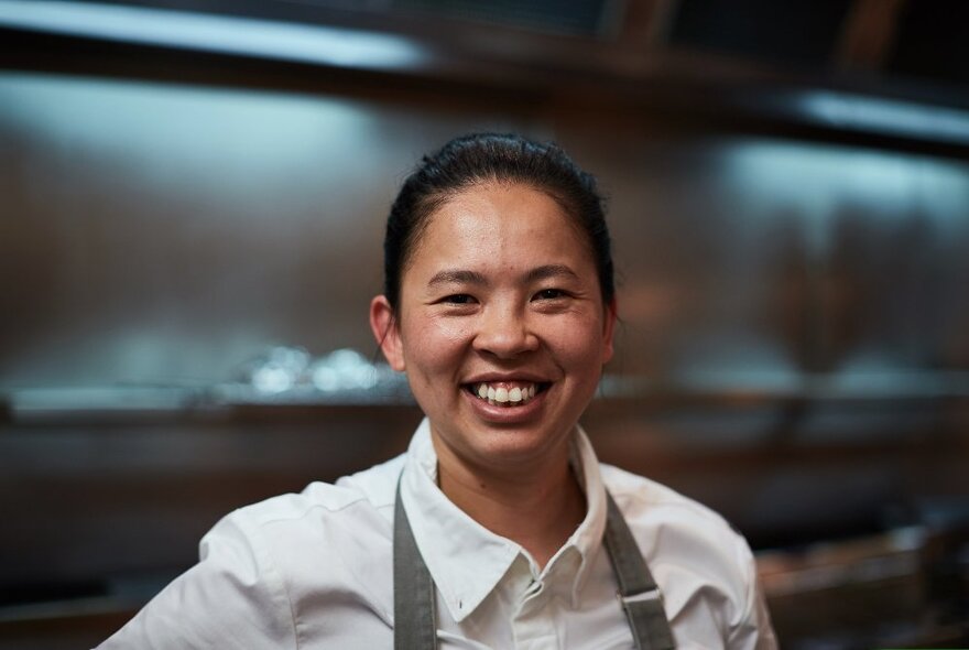 Smiling chef Thi Le, standing in a commercial kitchen.