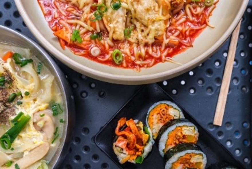 A selection of Korean dishes, including a spicy noodle dish, an umami broth and sliced gimbap.