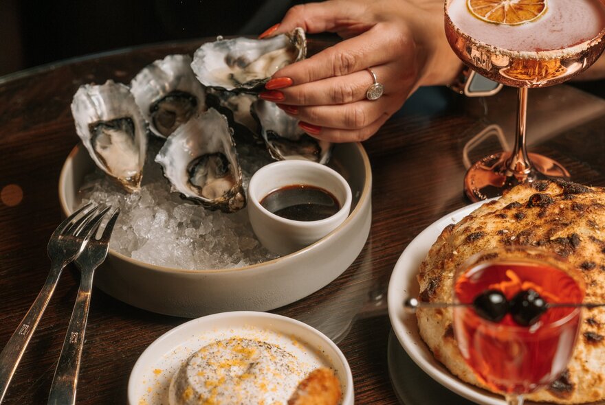 A table set with various dishes including 6 oysters and dipping sauce, puffed bread and cocktails. 