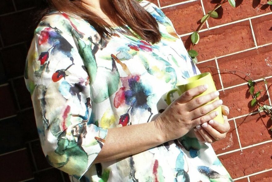 Woman wearing a multi-coloured top posing against a red-brick wall.