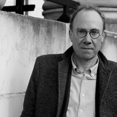 Black and white portrait of author and historian, Ben Macintyre, wearing glasses and a tweed jacket.