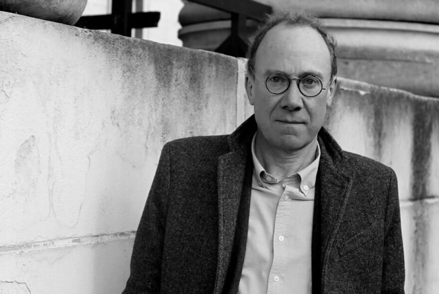 Black and white portrait of author and historian, Ben Macintyre, wearing glasses and a tweed jacket.